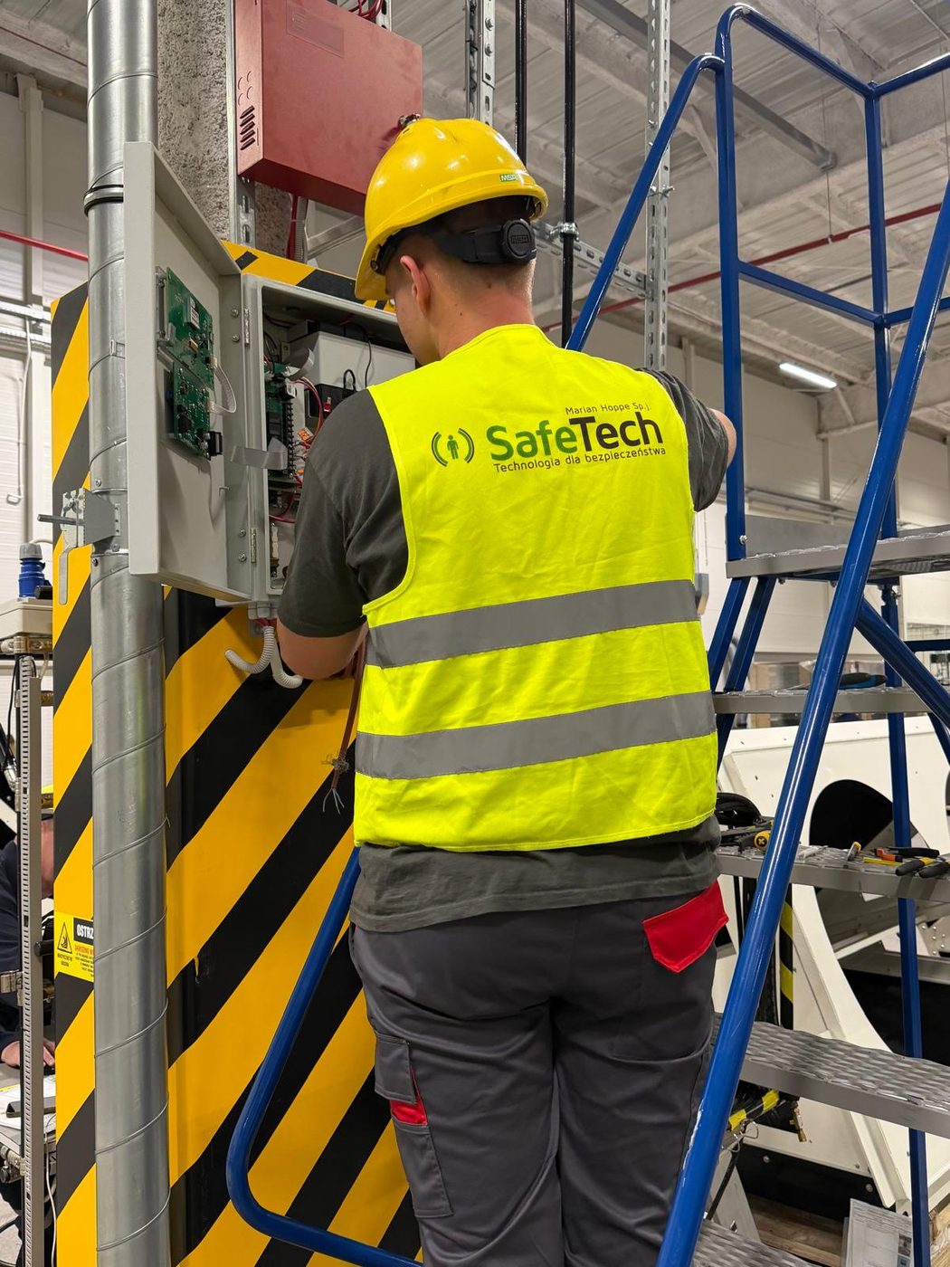 Technik SafeTech przy otwartej szafce sterowniczej systemu detekcji gazu podczas montażu w hali przemysłowej